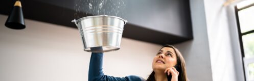 Woman holding bucket under leak in ceiling