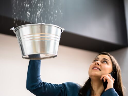 Woman holding bucket under leak in ceiling